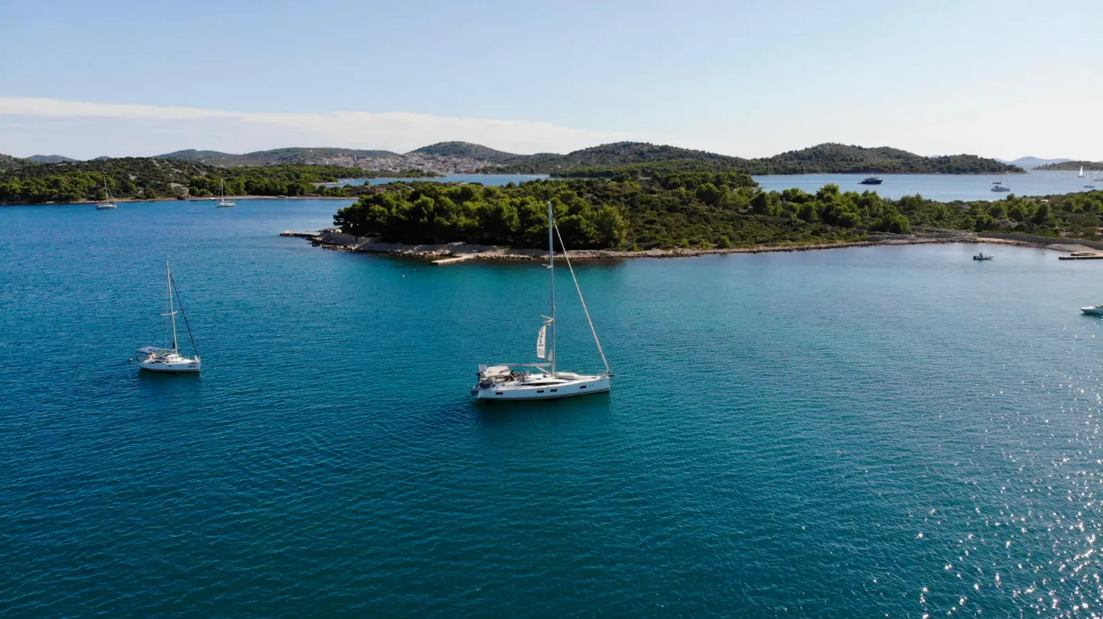 Two sailing yachts at anchor in a turquoise bay near Pirovac
